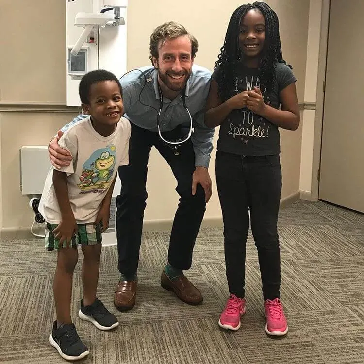 Dr. MacKenzie Farnham smiling with two young patients in the office.