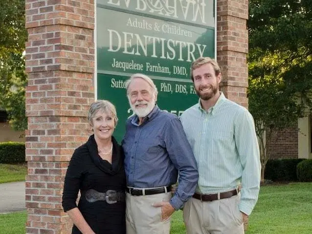 Drs. Jacquelene, Sutton and MacKenzie Farnham in front of the Farnham Dentistry sign.