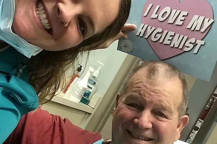 A Farnham Dentistry hygienist and a patient smiling, holding an I love my hygienist sign.